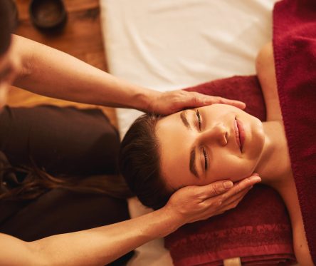 Calm Caucasian woman lying with closed eyes while massage practitioner putting palms on both sides of her face